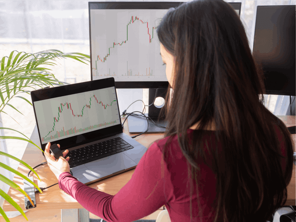 A woman is looking at a chart across her laptop and second monitor.