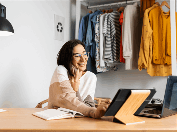 A woman is smiling whilst talking on the phone and using her laptop.