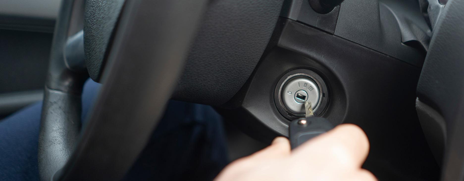 Eine Person steckt den Autoschlüssel in das Zündschloss eines Autos.