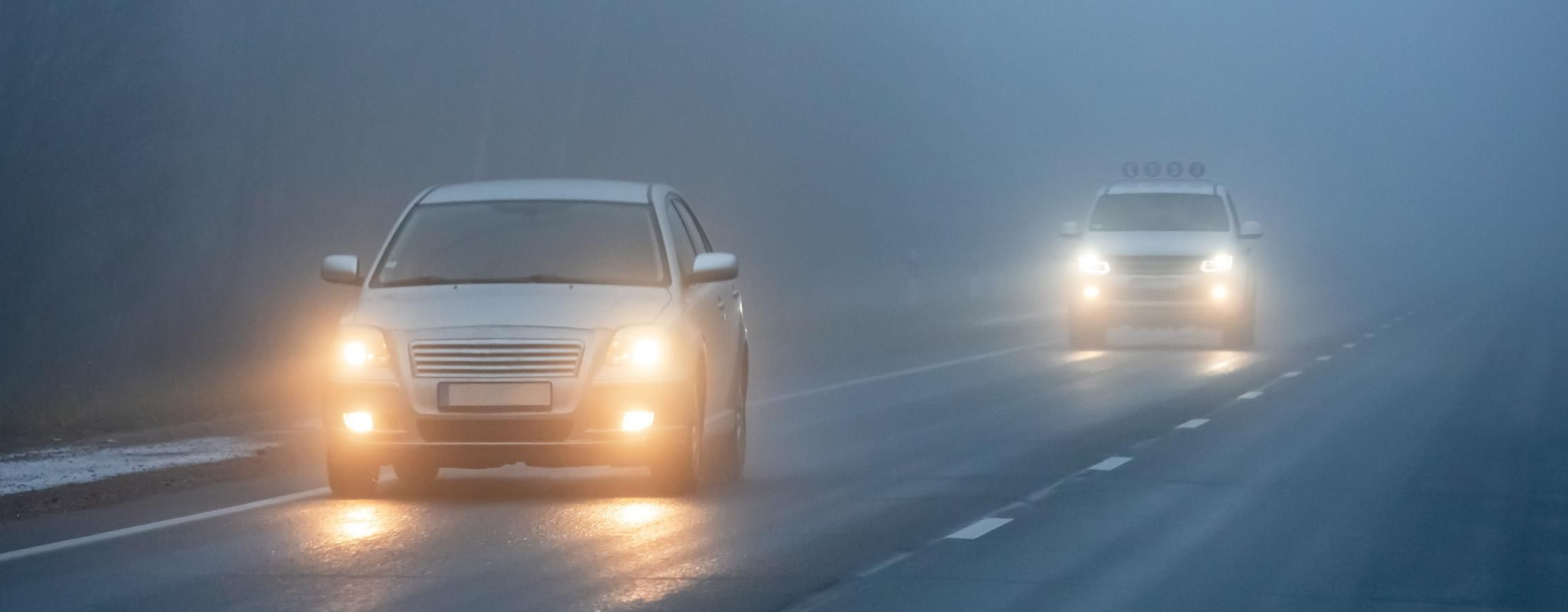 Zwei PKWs mit eingeschalteten Nebelscheinwerfern fahren auf einer Straße mit schlechten Sichtverhältnissen.