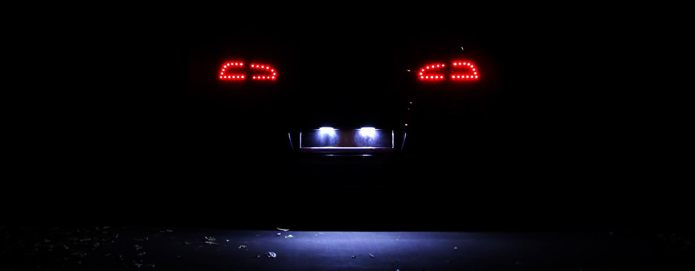 Ein dunkles Auto von hinten mit eingeschaltetem Rücklicht und beleuchtetem Kennzeichen