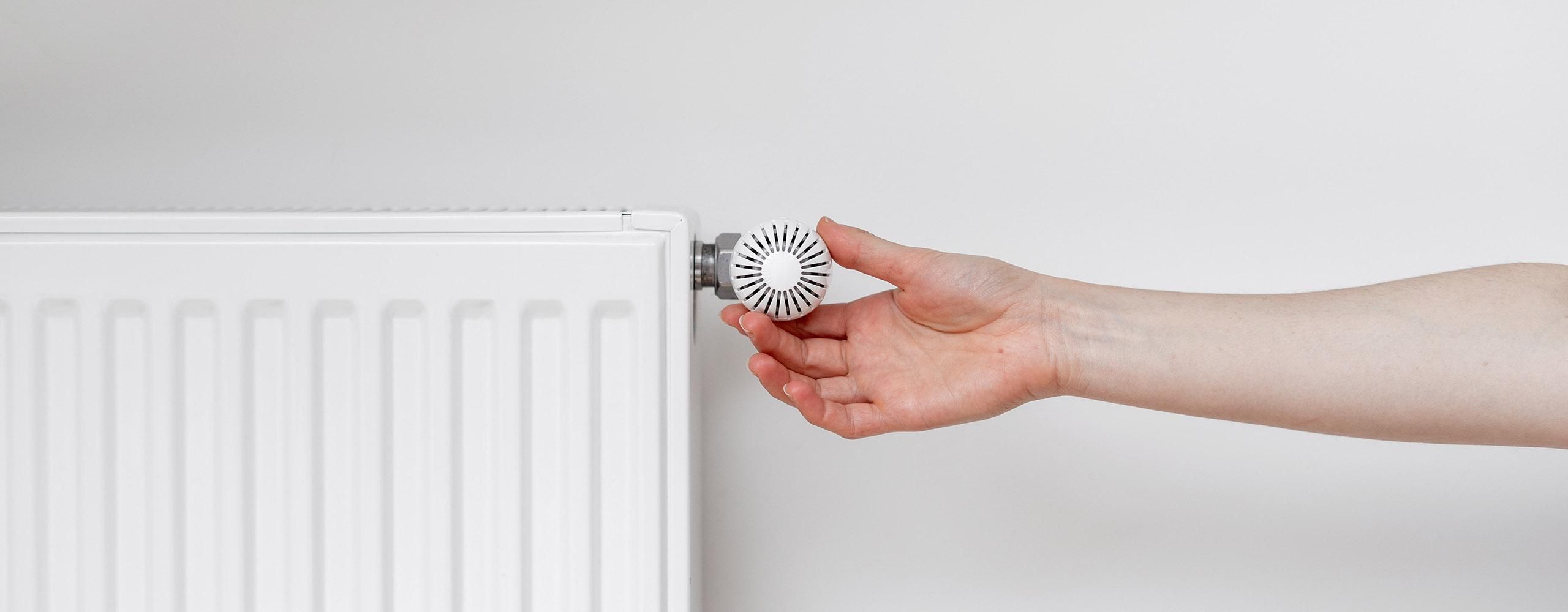 Eine Hand dreht am Thermostat einer Heizung.