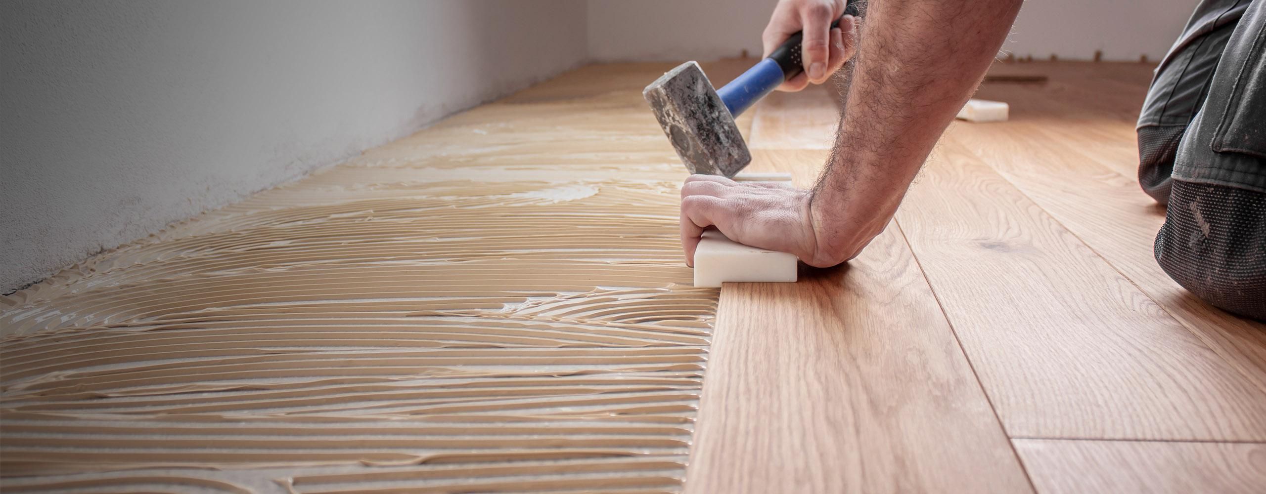 Ein Handwerker klebt Parkettdielen mit Kleber auf den Unterboden.