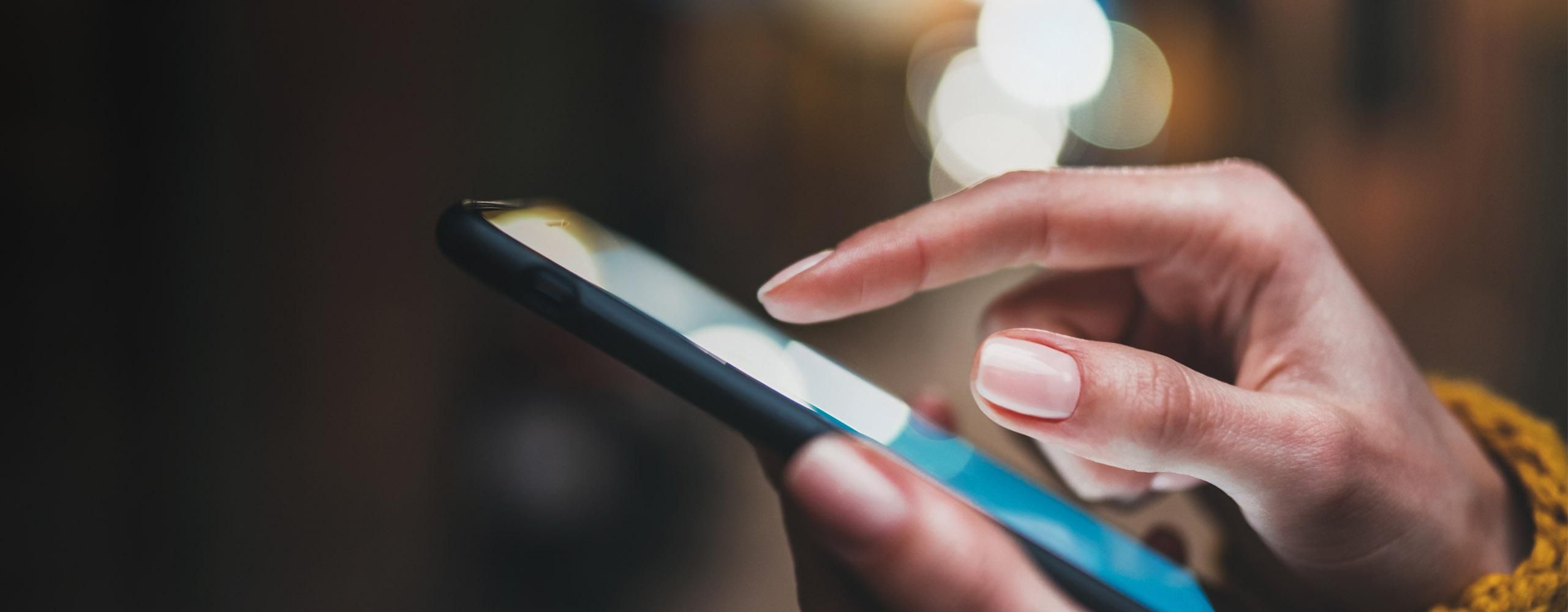 Ein Smartphone von der Seite, das von zwei Händen gehalten und bedient wird.