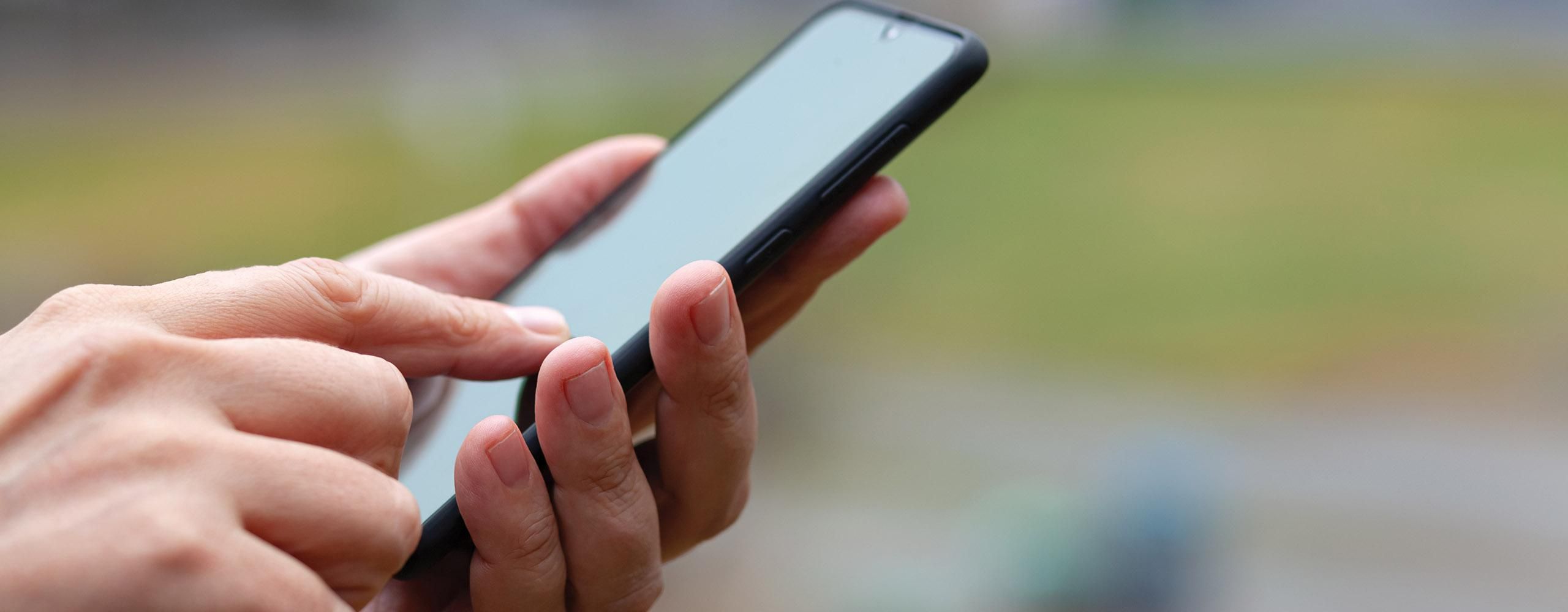 Nähere Aufnahme von einer Hand, die ein Smartphone hält, während die zweite Hand es bedient.