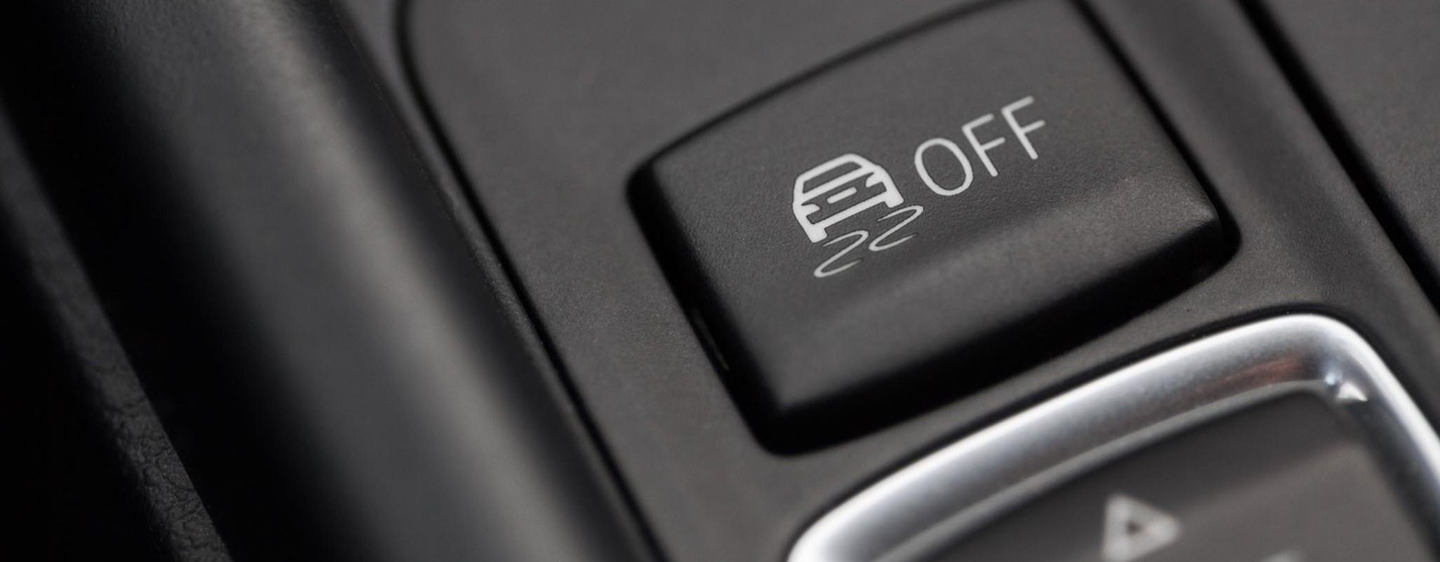 Nahaufnahme eines schwarzen ESP-Knopfs im Auto, der ein stilisiertes Fahrzeug mit geschwungenen Linien sowie die Beschriftung zeigt „Off“ zeigt.