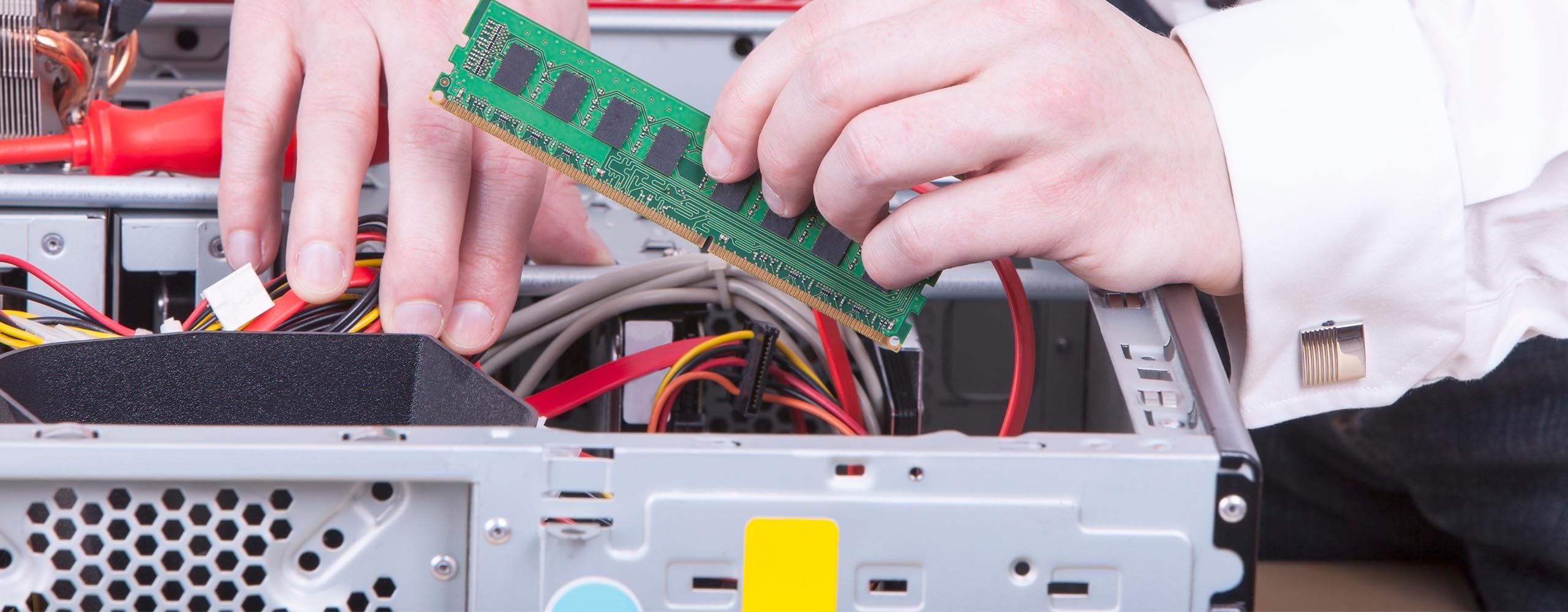 Eine Person setzt mit zwei Händen einen RAM-Riegel in einen geöffneten PC-Tower ein.