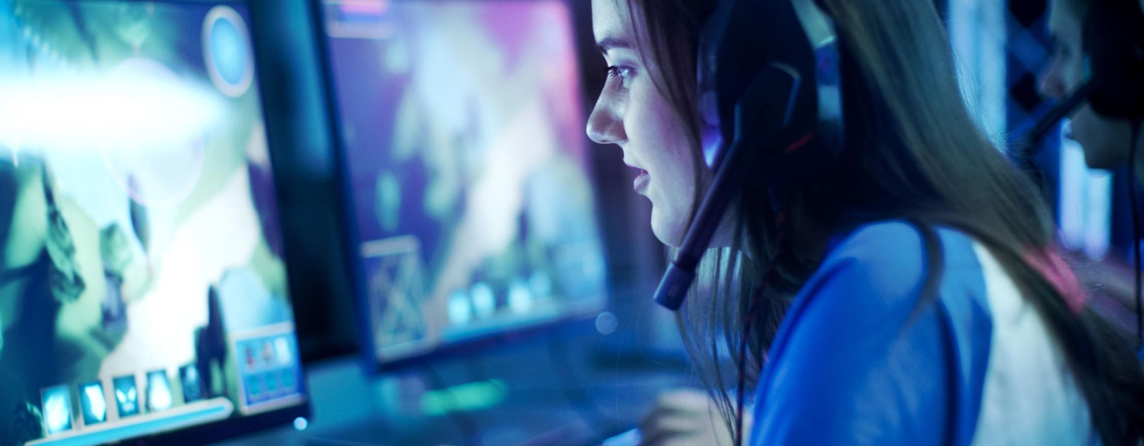 Zwei Personen sitzen an zwei Rechnern und spielen das gleiche Videospiel. Sie bedienen beide Maus und Tastatur und haben ein Headset auf.