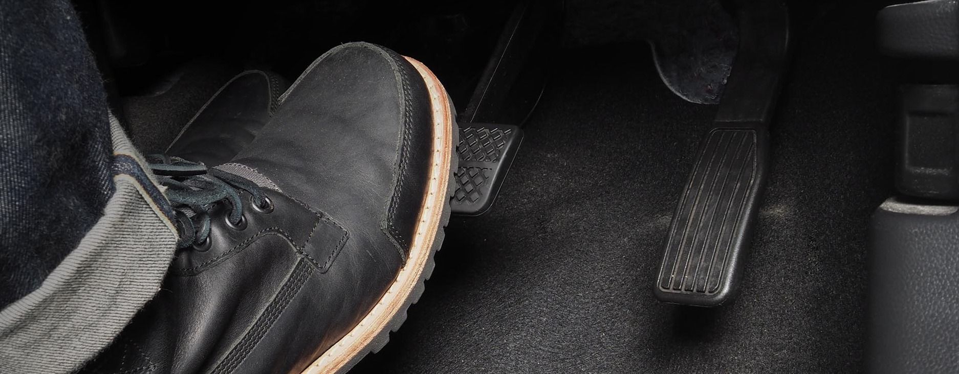 Ansicht auf einen gestiefelten Fuß, der das Bremspedal in einem Auto betätigt