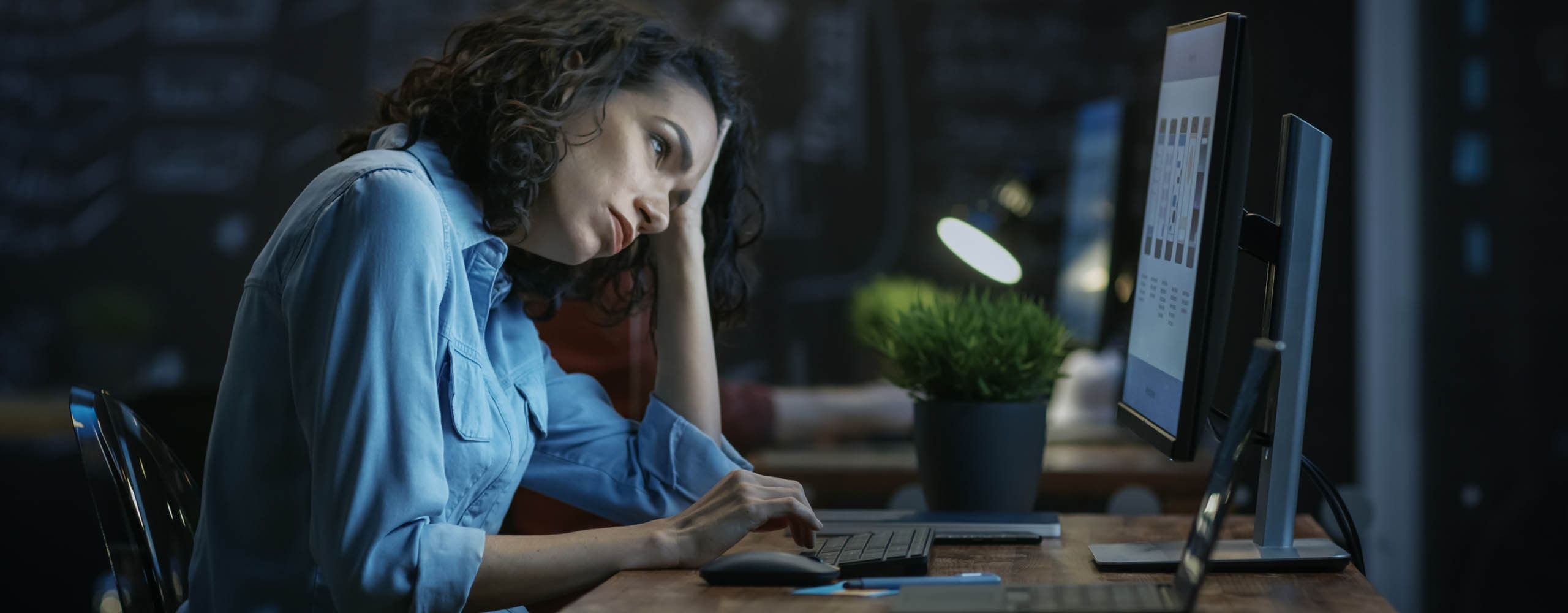 Eine Frau blickt anscheinend genervt auf einen Computer-Monitor und hält ihren Kopf mit dem aufgestützten Arm.
